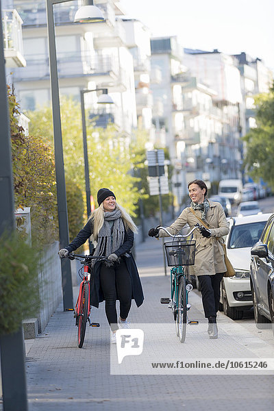 Frauen zu Fuß mit Fahrrädern in der Stadt