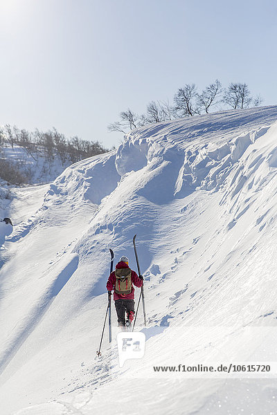 Mann trägt Skier einen verschneiten Hang hinauf