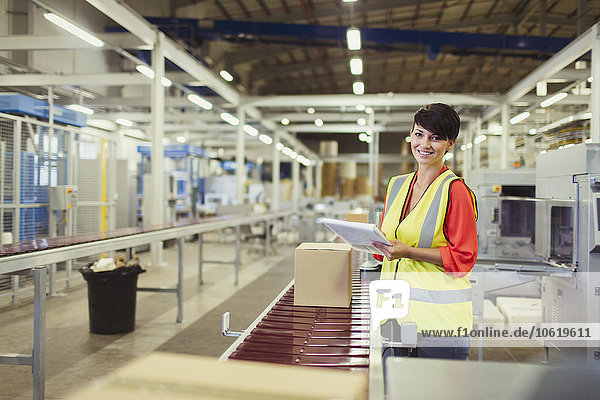 Portrait lächelnder Arbeiter beim Kontrollieren von Kartons auf der Förderband-Produktionslinie in der Fabrik