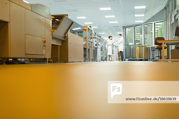 Arbeiter im Gespräch in der Nähe von Maschinen in der Druckerei