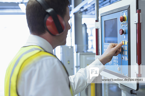 Arbeiter mit Gehörschutz am Bedienpult der Maschine
