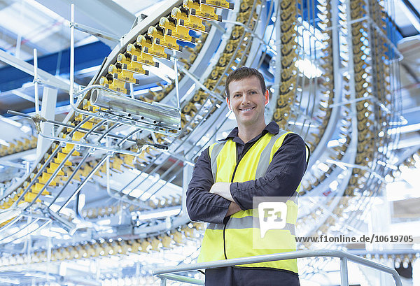 Porträtbewusster Arbeiter, der unter den Förderbändern der Druckmaschine steht.