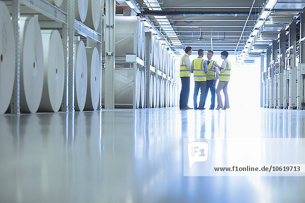 Arbeiter sprechen in der Nähe von großen Papierrollen in der Druckerei