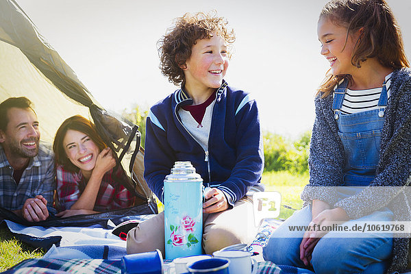 Lächelnde Geschwister mit isoliertem Getränkebehälter auf dem Campingplatz