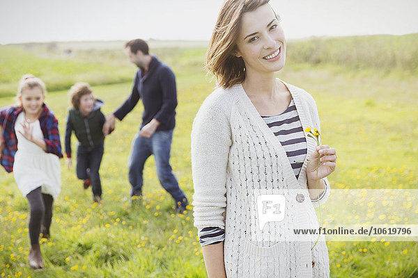 Portrait lächelnde Frau hält Wildblume auf der Wiese mit Familie