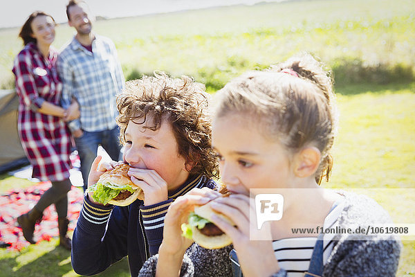 Geschwister essen Hamburger auf dem sonnigen Campingplatz