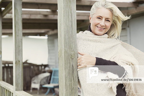 Portrait lächelnde Seniorin mit Schal auf windigem Vorbau