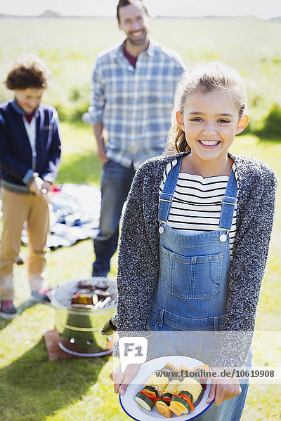 Portrait lächelndes Mädchen mit Gemüsespießen auf dem sonnigen Campingplatz