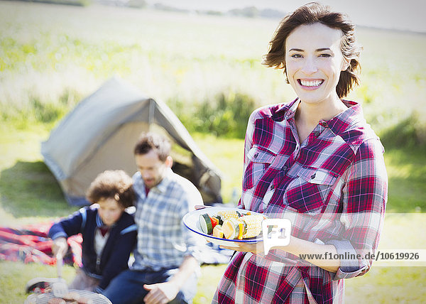 Portrait lächelnde Frau mit Gemüsespießen auf dem sonnigen Campingplatz