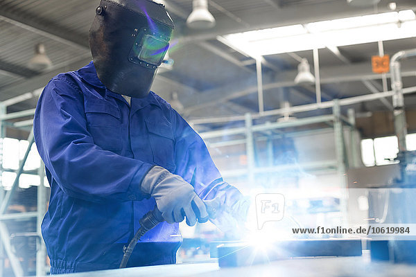 Welder in protective workwear using welding torch in steel factory