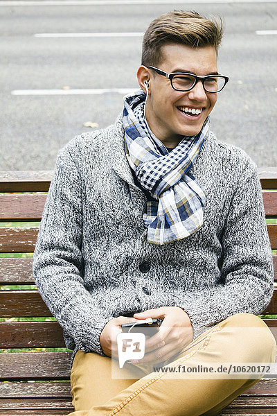 Portrait of smiling teenage boy sitting on a bench hearing music with earphones