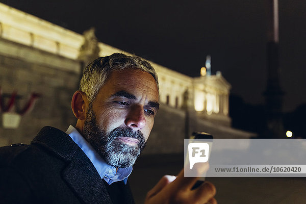 Österreich  Wien  Porträt eines Mannes vor dem Parlamentsgebäude mit Blick auf sein Smartphone bei Nacht