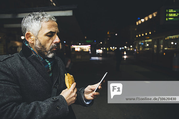 Österreich  Wien  Mann mit Käse-Karniolan-Wurst beim Blick auf sein Smartphone bei Nacht
