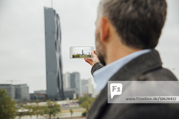 Österreich  Wien  Geschäftsmann beim Fotografieren von DC Towers mit seinem Smartphone