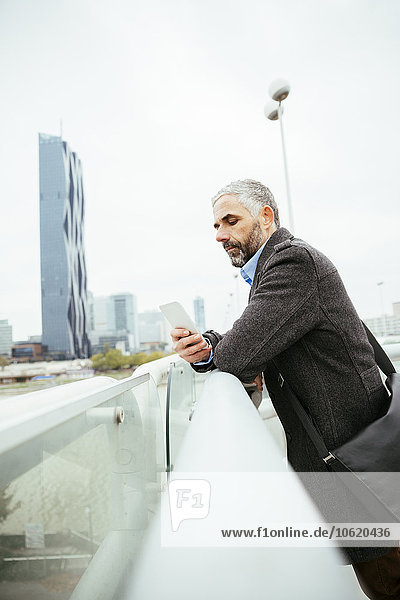 Österreich  Wien  Geschäftsmann auf der Reichsbrücke mit Blick auf sein Smartphone