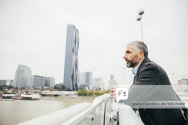 Österreich  Wien  Geschäftsmann mit Smartphone auf der Reichsbrücke mit Blick auf die Ferne