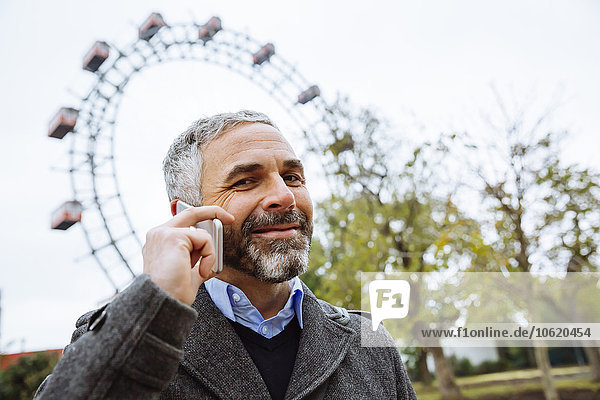 Österreich  Wien  Porträt eines lächelnden Geschäftsmannes beim Telefonieren mit dem Smartphone im Prater