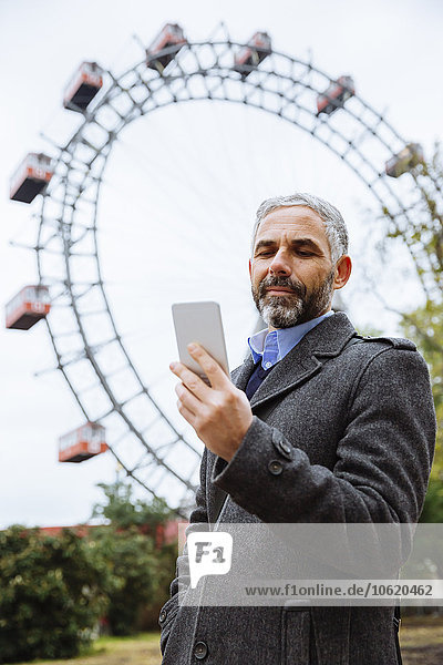 Österreich  Wien  Porträt eines Geschäftsmannes mit Blick auf sein Smartphone im Prater