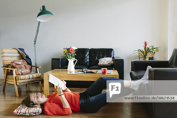 Junge Frau auf dem Boden ihres Wohnzimmers liegend mit digitalem Tablett