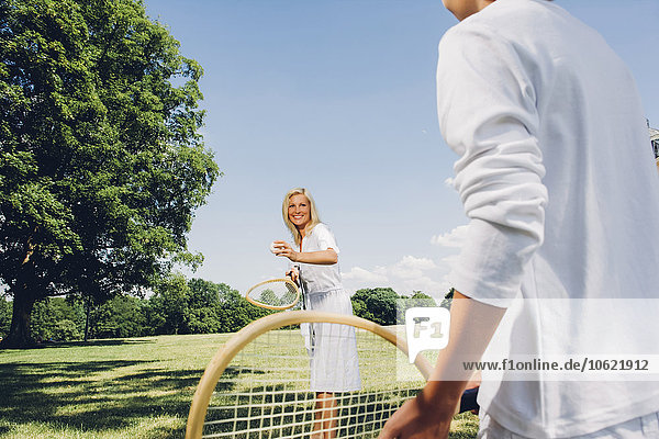 Frau spielt mit ihrem Sohn Tennis an einem Sommertag im Park.