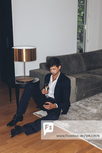 Young man with glass of champagne looking on cell phone