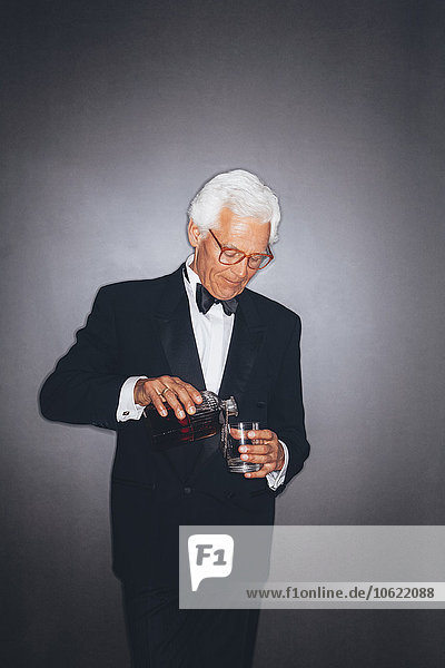 Elegant senior man pouring drink into tumbler