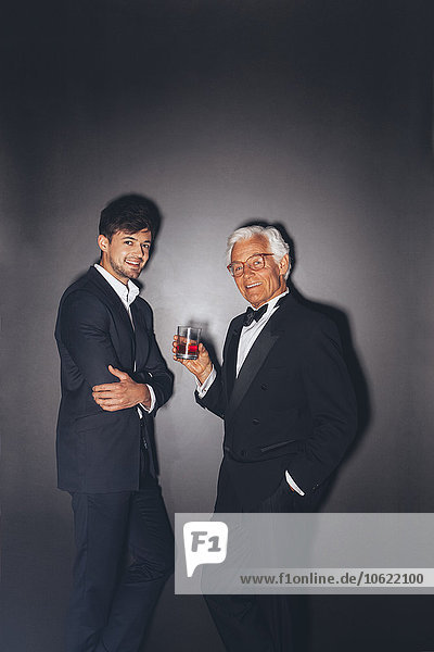 Smiling young man and elegant senior man holding drink