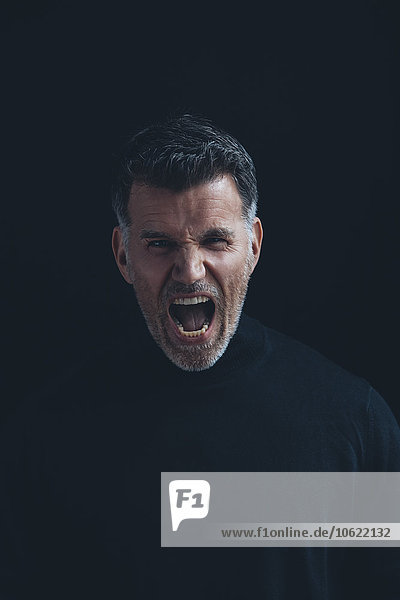 Porträt eines schreienden Mannes mit schwarzem Rollkragenpulli vor schwarzem Hintergrund