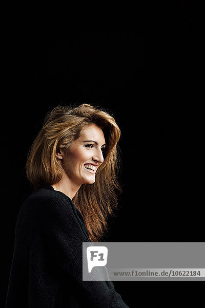 Portrait of smiling woman with brown hair wearing black clothes in front of black background