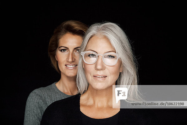 Portrait of mature woman and younger woman standing behind her in front of black background
