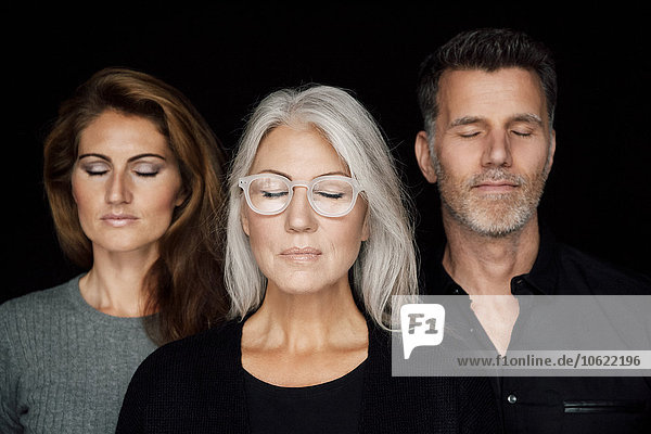Porträt von drei Personen mit geschlossenen Augen vor schwarzem Hintergrund