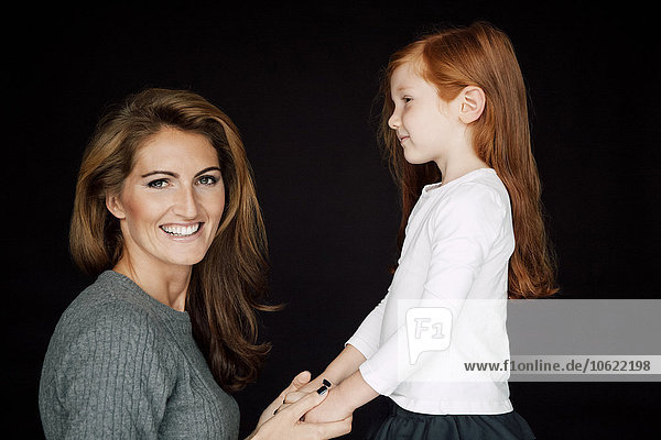 Mother and little daughter holding hands in front of black background