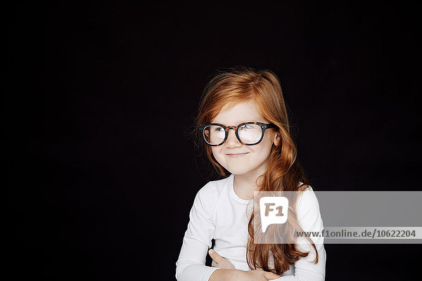 Portrait of redheaded smiling little girl wearing oversized glasses in front of black background