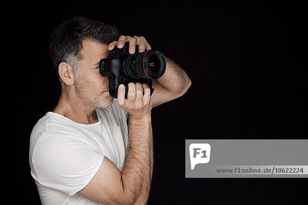 Man photographing with camera in front of black background