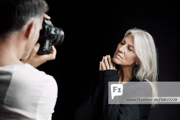 Mann fotografiert Frau vor schwarzem Hintergrund