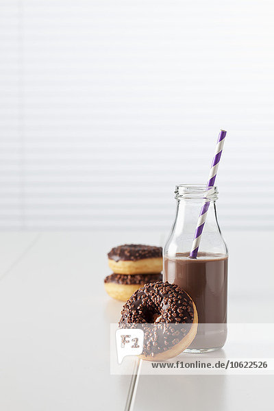 Glasflasche Kakao und drei Donuts mit Schokoladenglasur auf weißem Grund