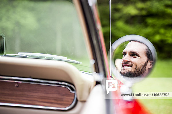 Reflection of smiling young man in wing mirror of convertible