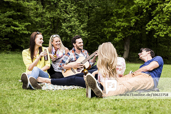 Happy friends with guitar and beer bottles relaxing in park