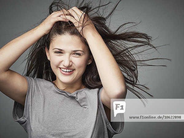 Porträt der glücklichen brünetten jungen Frau mit den Händen im Haar
