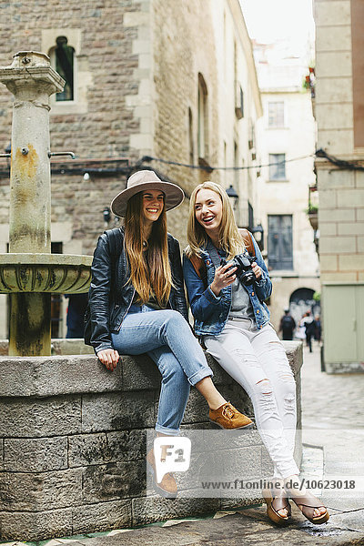 Spanien  Barcelona  zwei glückliche junge Frauen an einem Brunnen