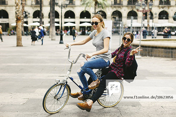 Spain  Barcelona  two happy young women sharing bicycle in the city