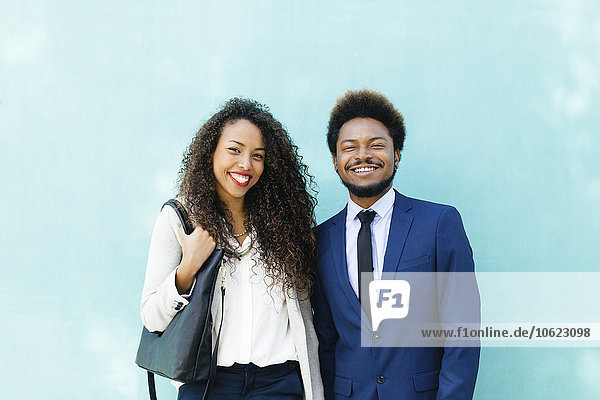 Porträt von zwei lächelnden jungen Geschäftsleuten vor der blauen Wand