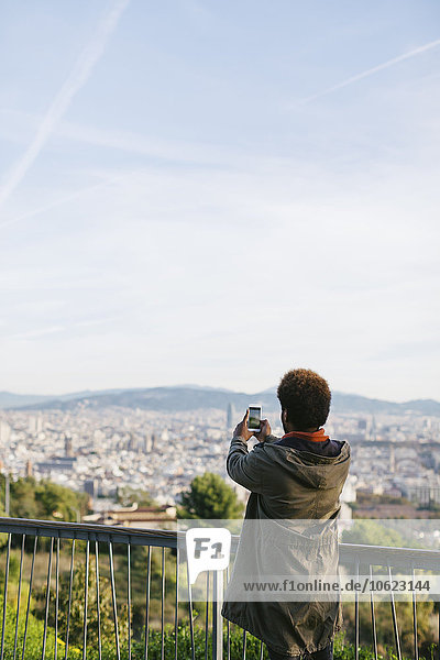 Spanien  Barcelona  Rückansicht eines jungen Mannes  der mit seinem Smartphone fotografiert.