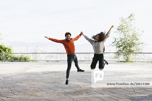 Spanien  Barcelona  Portrait eines glücklichen jungen Paares  das auf der Aussichtsterrasse in die Luft springt.