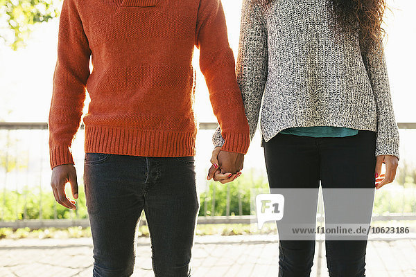 Young couple wearing knit pullovers standing side by side holding hands  partial view