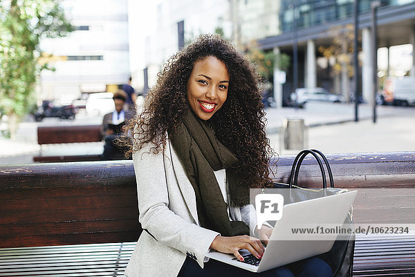 Smiling young woman using laptop on bench