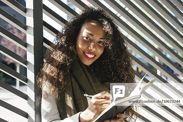 Porträt einer lächelnden jungen Frau mit Notizbuch im Freien