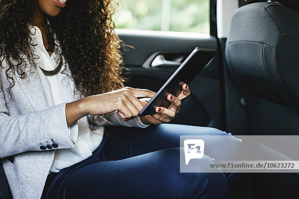 Young woman sitting on back seat of a car using mini tablet  close-up