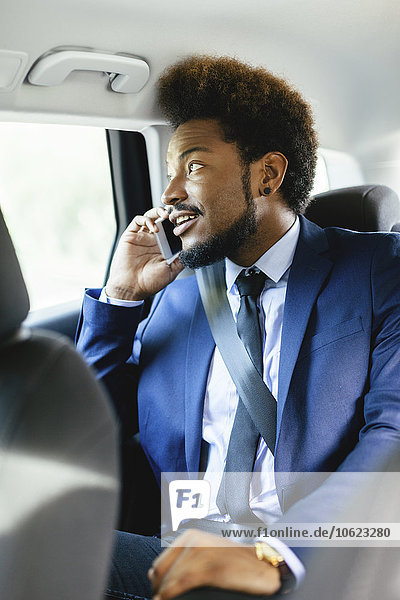 Geschäftsmann sitzt auf dem Rücksitz eines Autos und telefoniert mit dem Smartphone.