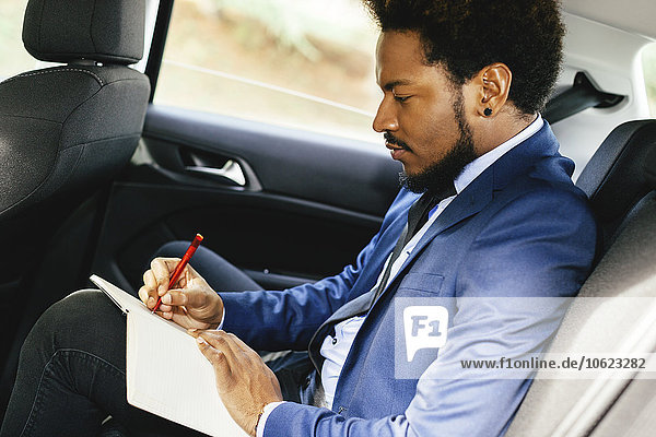 Geschäftsmann sitzt auf dem Rücksitz eines Autos und schreibt etwas auf.